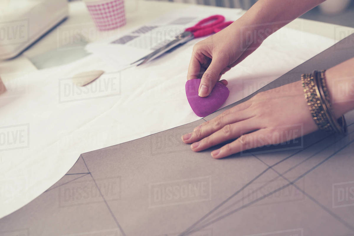 Closeup of the hands of a seamstress marking a fabric with a chalk