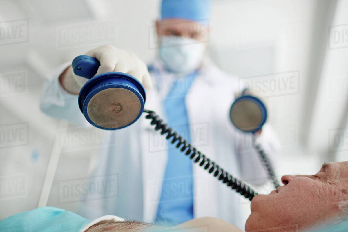 Doctor performing a defibrillator on patient in emergency room Stock