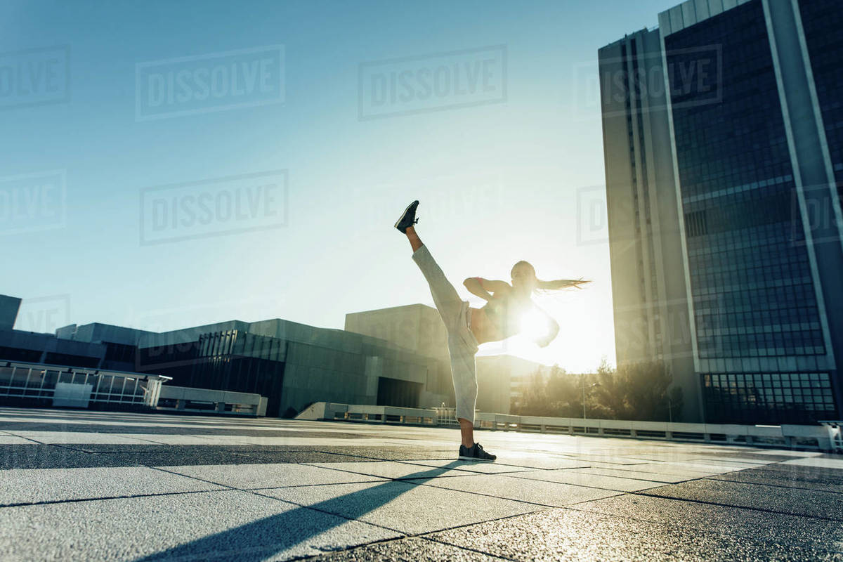 Urban woman doing high roundhouse kick outdoors in the city. Female practicing martial arts in a sunny day. Royalty-free stock photo