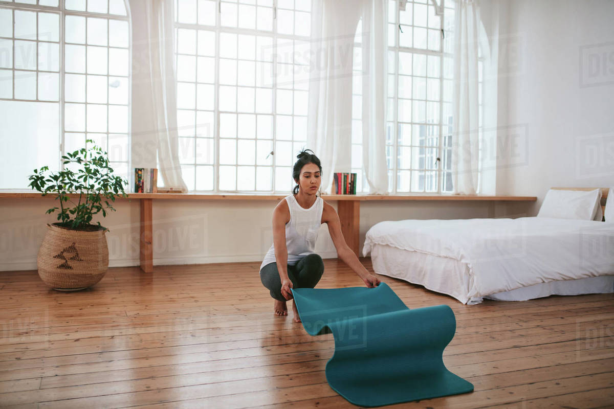 Indoor shot of fit young woman putting yoga mat on floor. Fitness