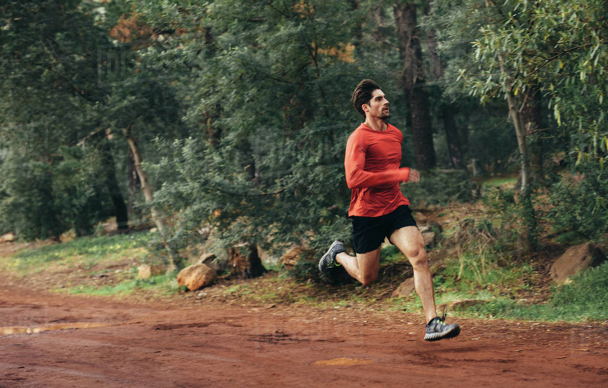Man running on mud track. Athlete running fast in a park with dense