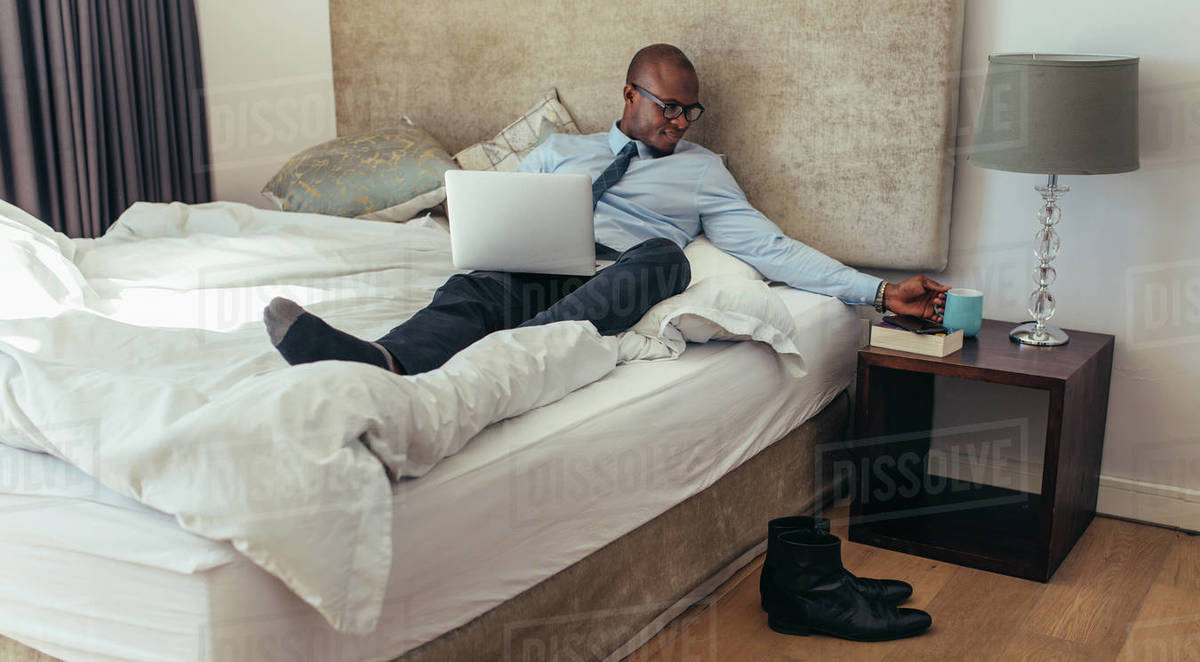 Confident man in formal clothes working on laptop while lying in bed