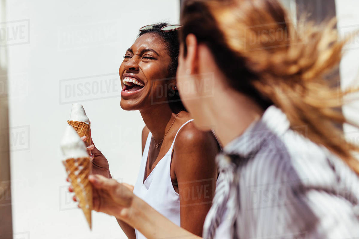 Two happy looking women eating ice cream cones on a sunny day outdoors