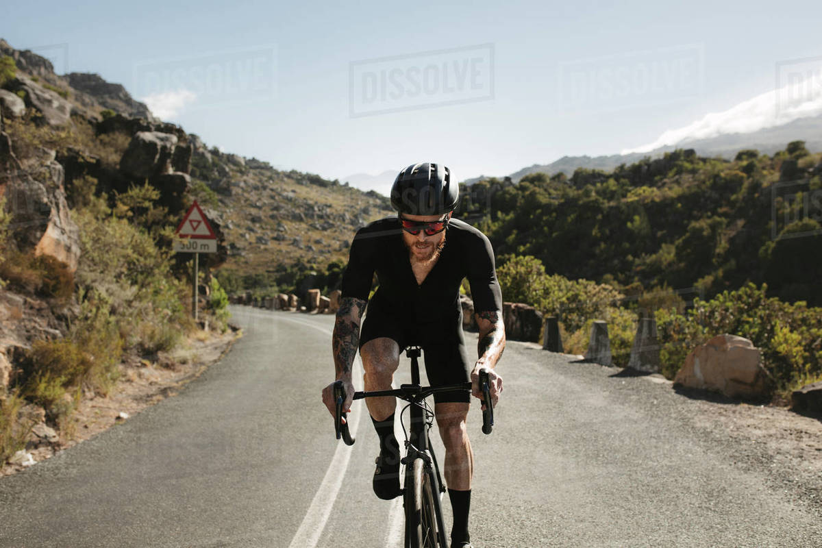 Professional bicycle rider doing uphill ride on mountain road. Sportsman climbing up the hill on