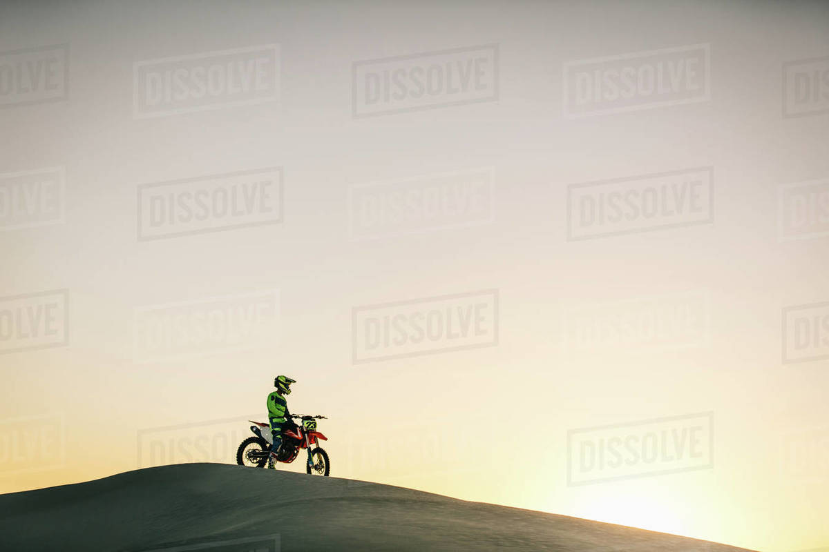 Motocross rider sitting on his bike on a sand dune. Motorcycle rider driving on the dunes during sunset. Royalty-free stock photo