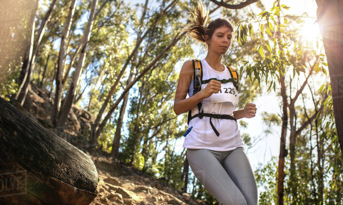 Fit young woman runner in sportswear running a mountain marathon with bright sunlight from the back. Fit trail runner running in a mountain race. Royalty-free stock photo