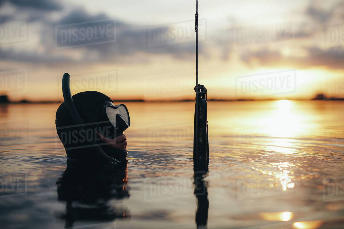 Image of male diver with speargun in water. Spearfishing in evening