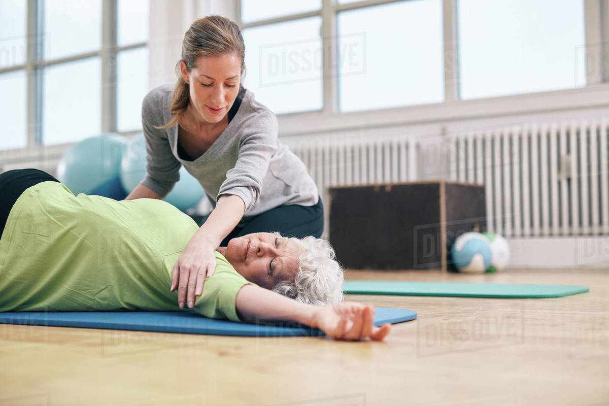 Senior women lying on exercise mat doing stretching workout for back