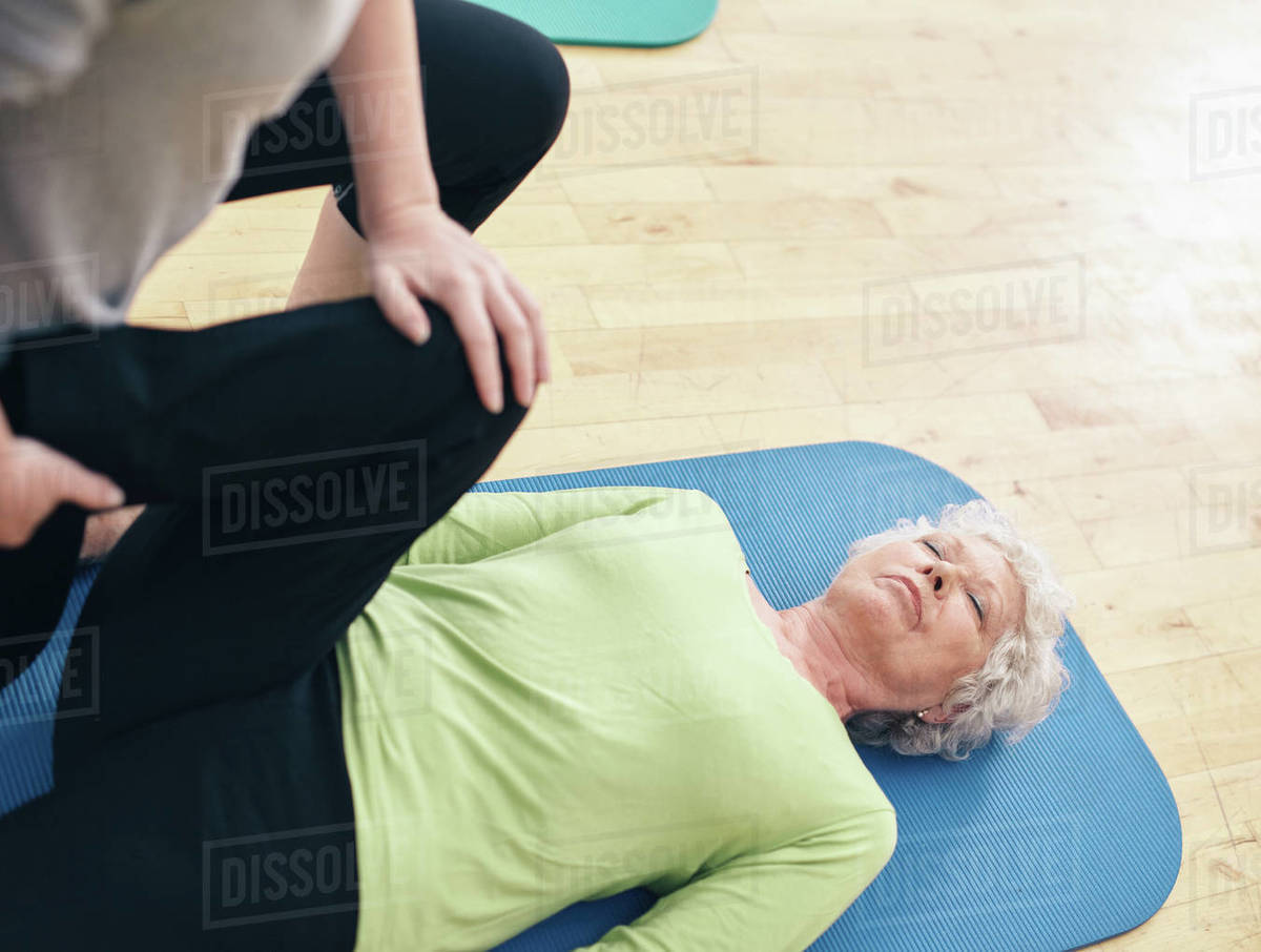 Senior woman lying on exercise mat with her personal trainer helping