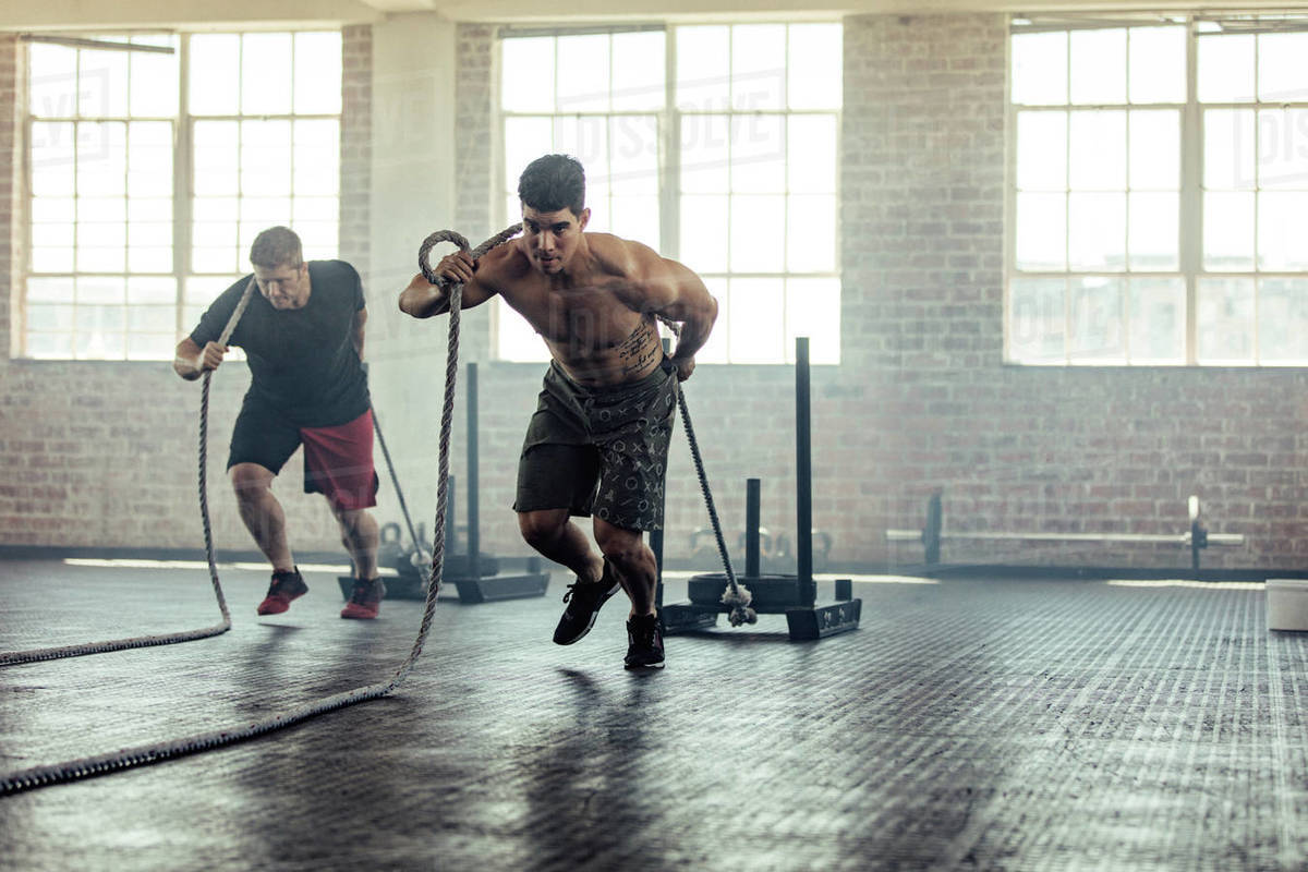 Shot of a determined young men pulling weights across the floor in a