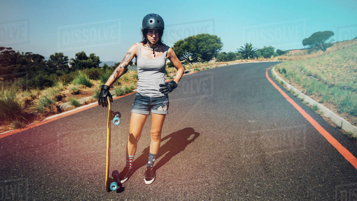 Full length portrait of young woman standing on a countryside highway with a longboard. Royalty-free stock photo