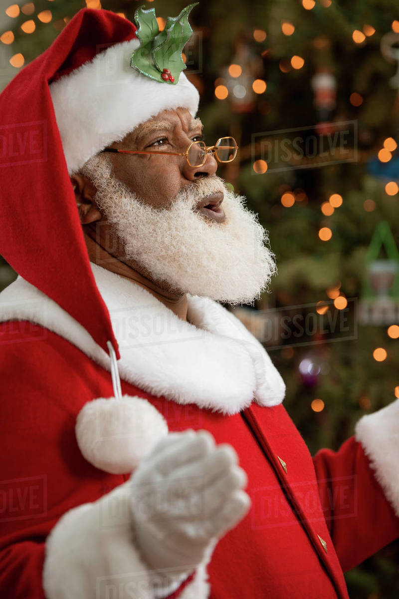 An African American man dressed as Santa Claus sitting in front of a Christmas tree laughing happily.  Royalty-free stock photo