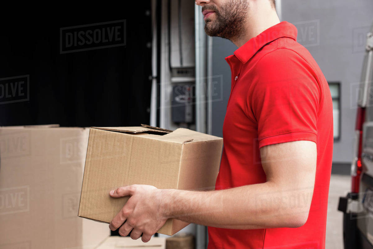 partial view of delivery man discharging cardboard boxes from van