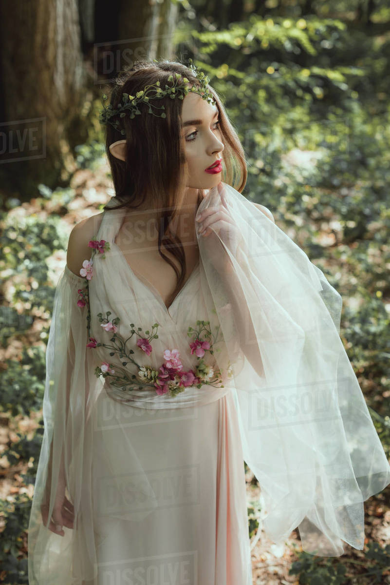 Mystic elf in elegant dress with flowers in forest - Royalty-free Stock Photo | Dissolve Mystic elf in elegant dress with flowers in forest - Royalty-free Stock Photo | Dissolve