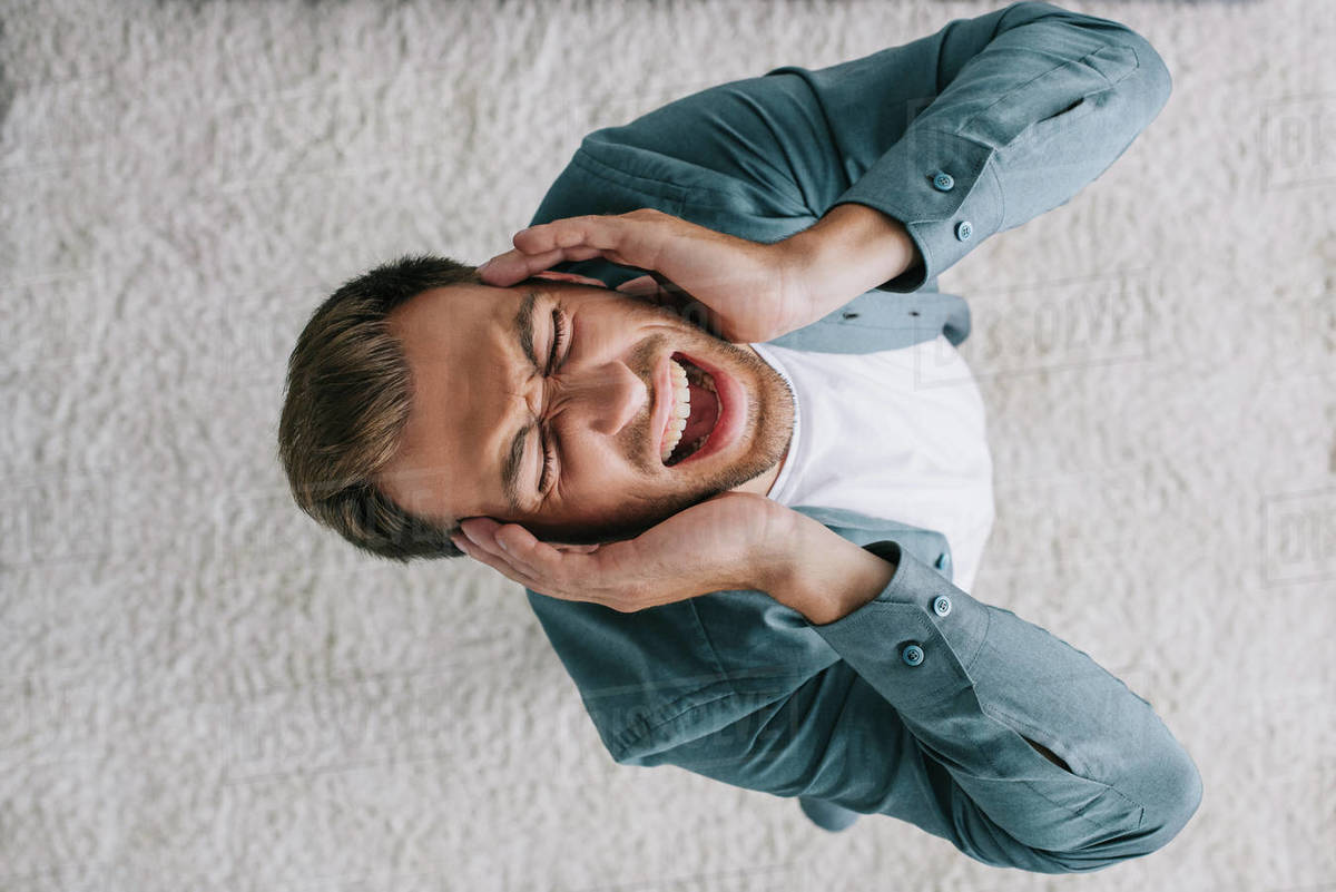 Overhead view of young man screaming and suffering from headache at home Stock Photo Dissolve