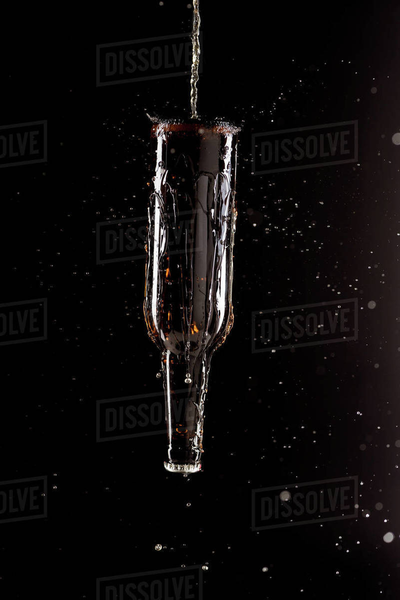Selective focus of beer pouring on bottle upside down with splashes