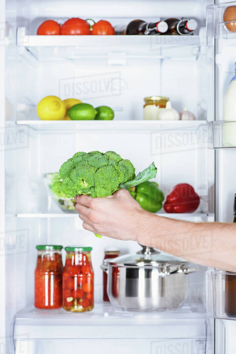 Cropped image of man taking broccoli from fridge Stock Photo Dissolve