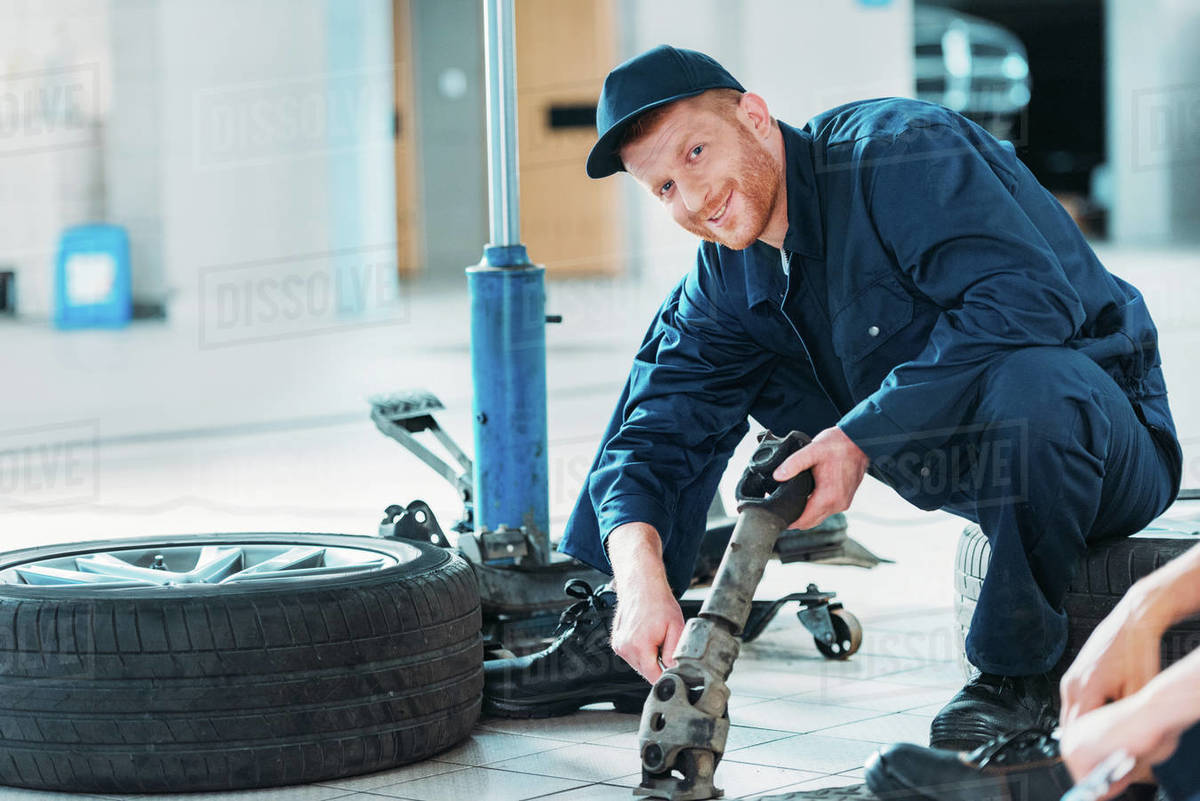 Automechanic holding a car part sitting on a floor at a repair shop