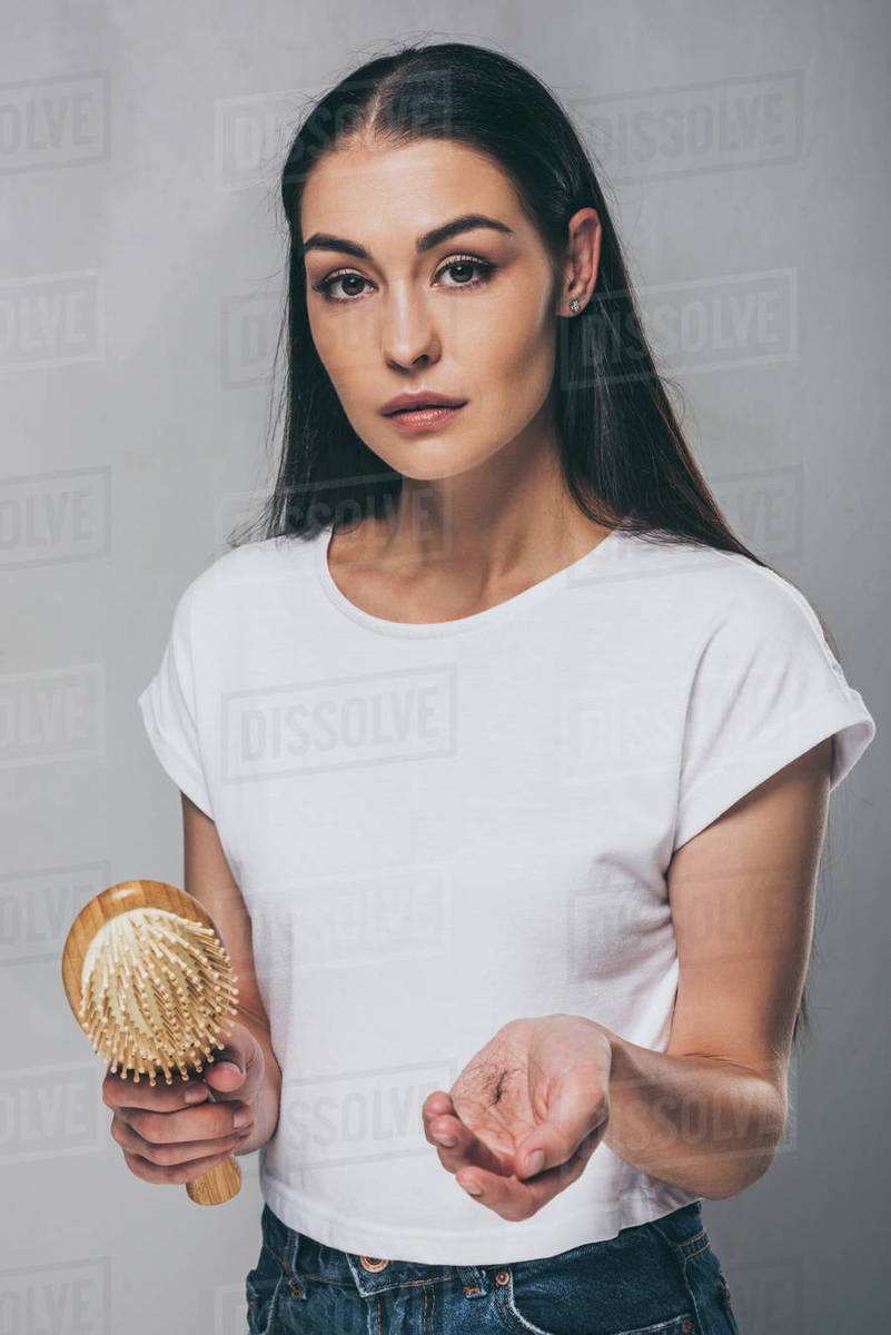 Young woman holding hairbrush with fallen hair and looking at camera