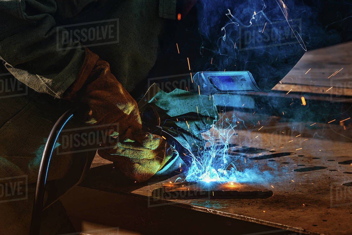 Partial view of welder in protection mask brazing metal at factory