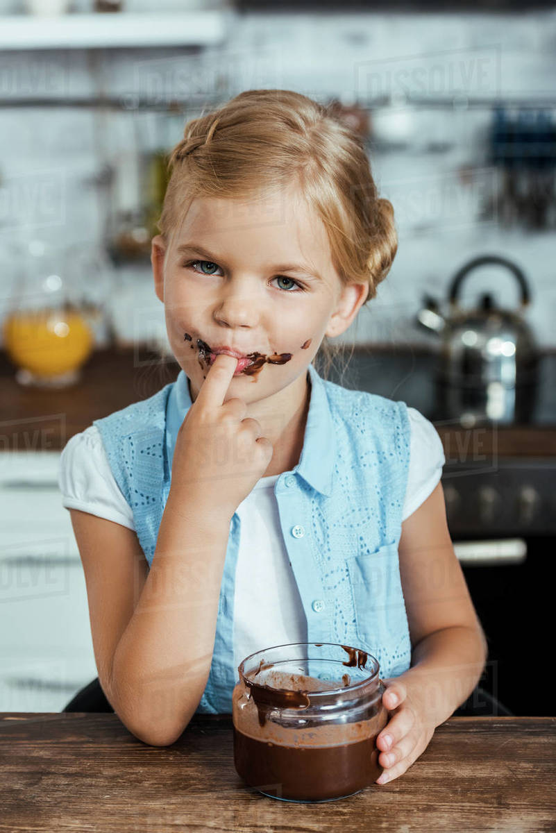 Adorable child eating delicious chocolate spread and smiling at camera