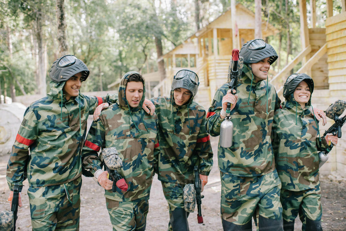 Laughing paintball players in camouflage with marker guns embracing