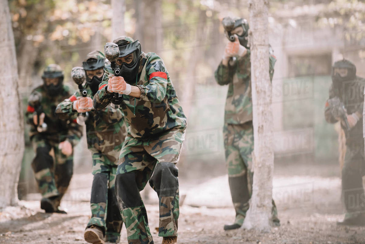 Paintball team in uniform and protective masks aiming by paintball guns