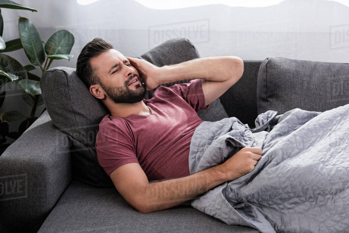 Suffering young man with headache lying on couch Stock Photo Dissolve