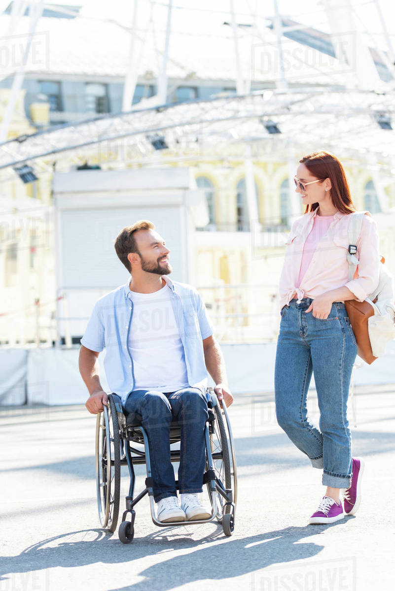 Smiling Handsome Boyfriend In Wheelchair And Girlfriend Looking At Each Other On Street Stock Photo Dissolve