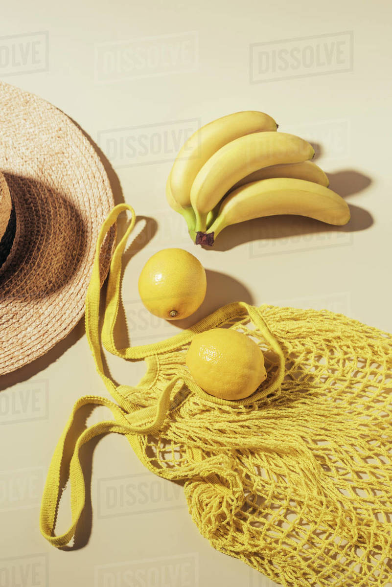 Top view of straw hat and yellow string bag with lemons and bananas Stock Photo Dissolve