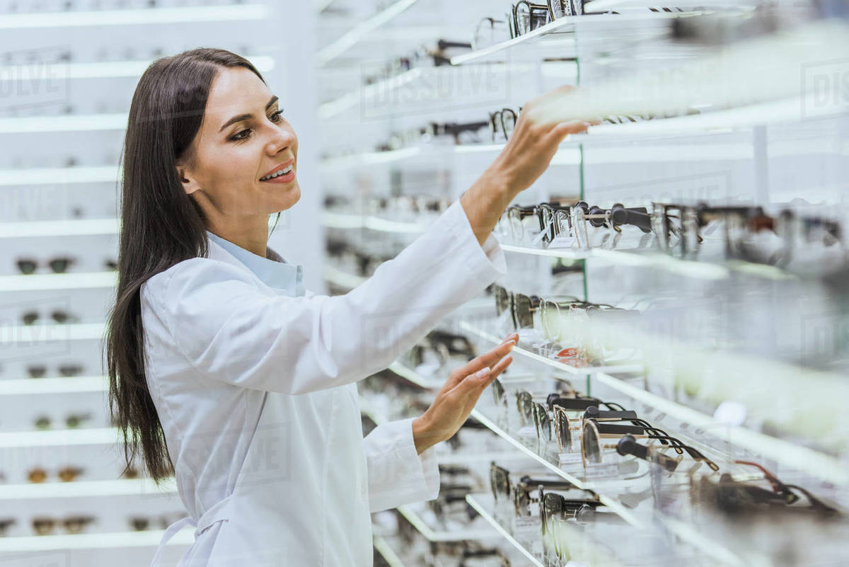 Professional smiling optician taking glasses from shelves in