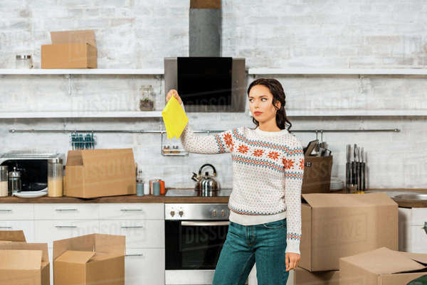young woman holding dirty yellow rag in kitchen with cardboard boxes at ...