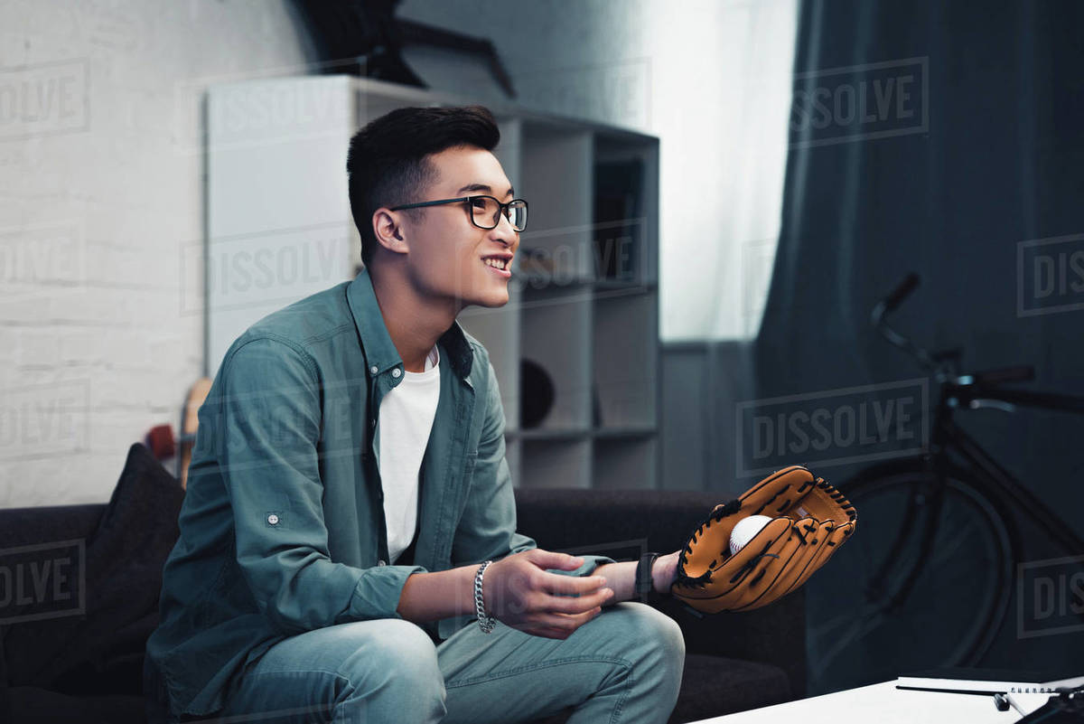 Smiling Young Asian Man With Baseball Glove And Ball Sitting On
