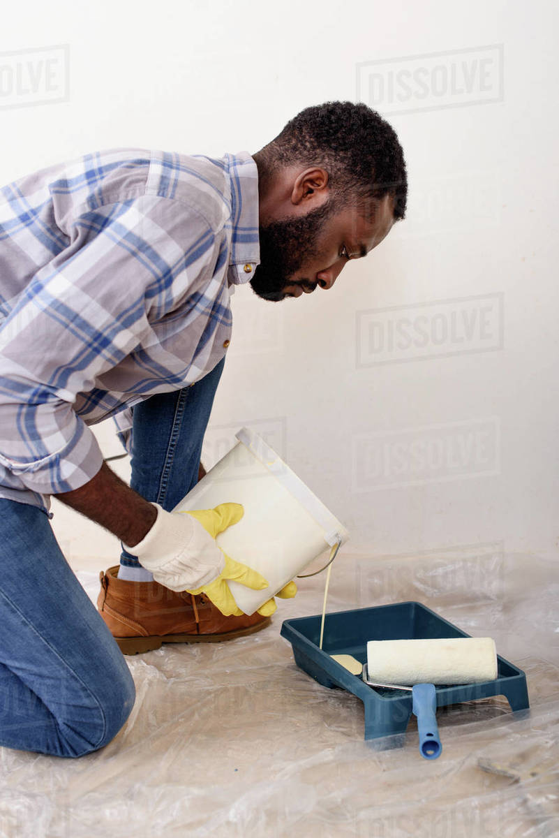 Focused African American man in protective gloves pouring paint into
