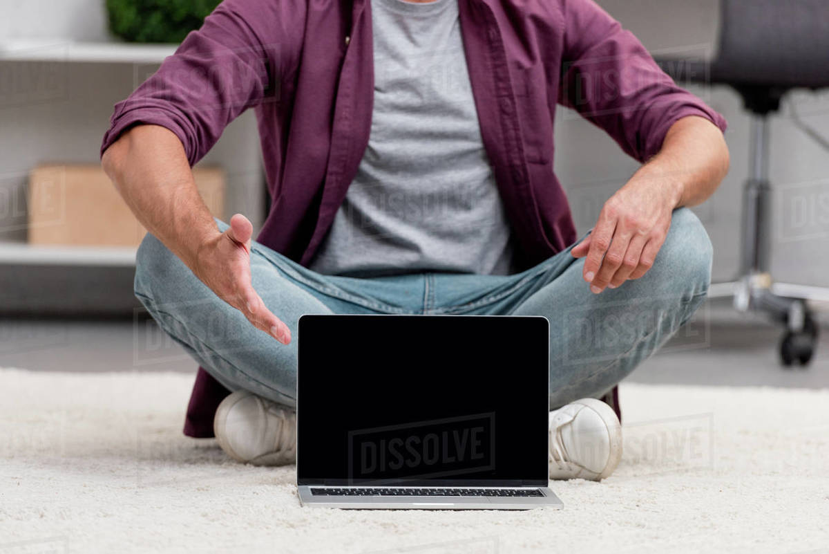 Cropped view of man sitting with laptop on carpet Stock Photo Dissolve