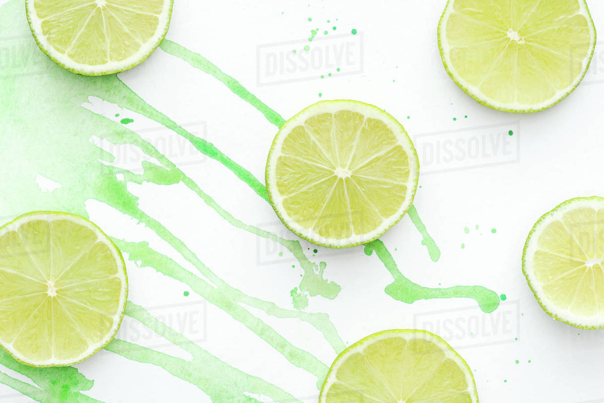 Top view of pieces of ripe raw limes on white surface with green