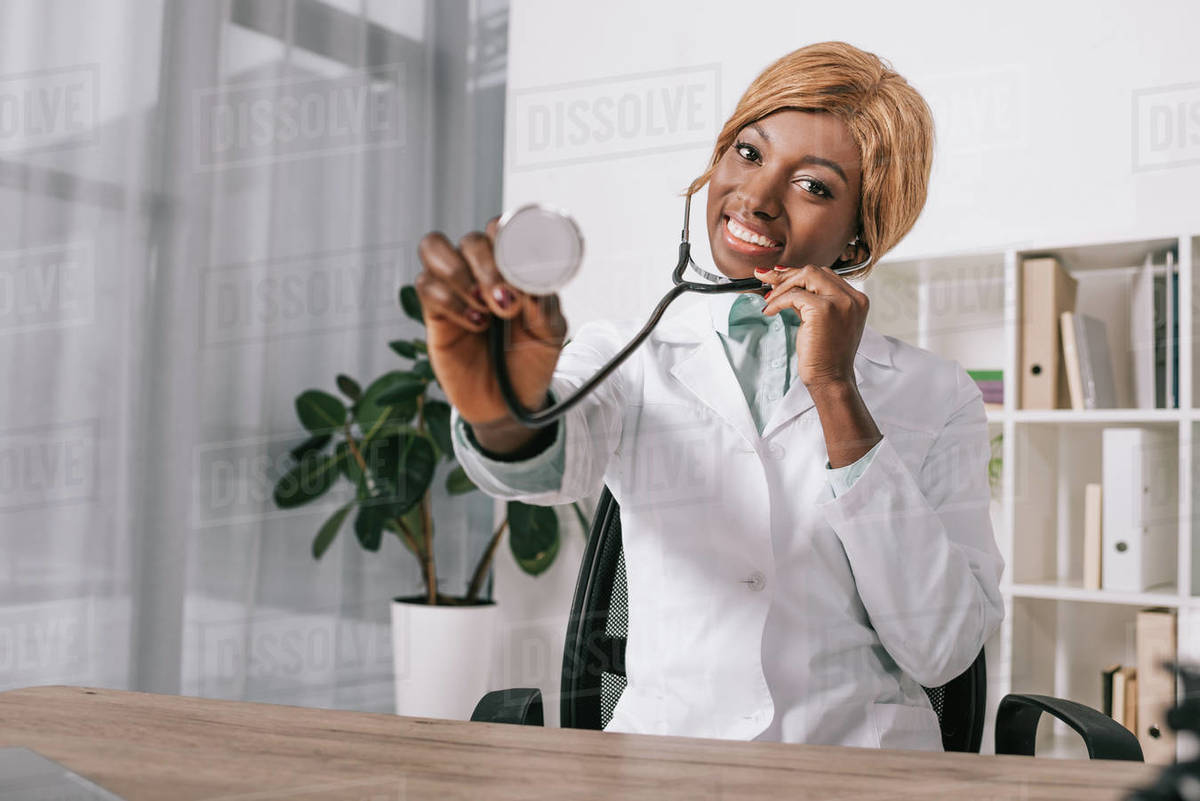 Smiling African American doctor showing stethoscope while sitting in