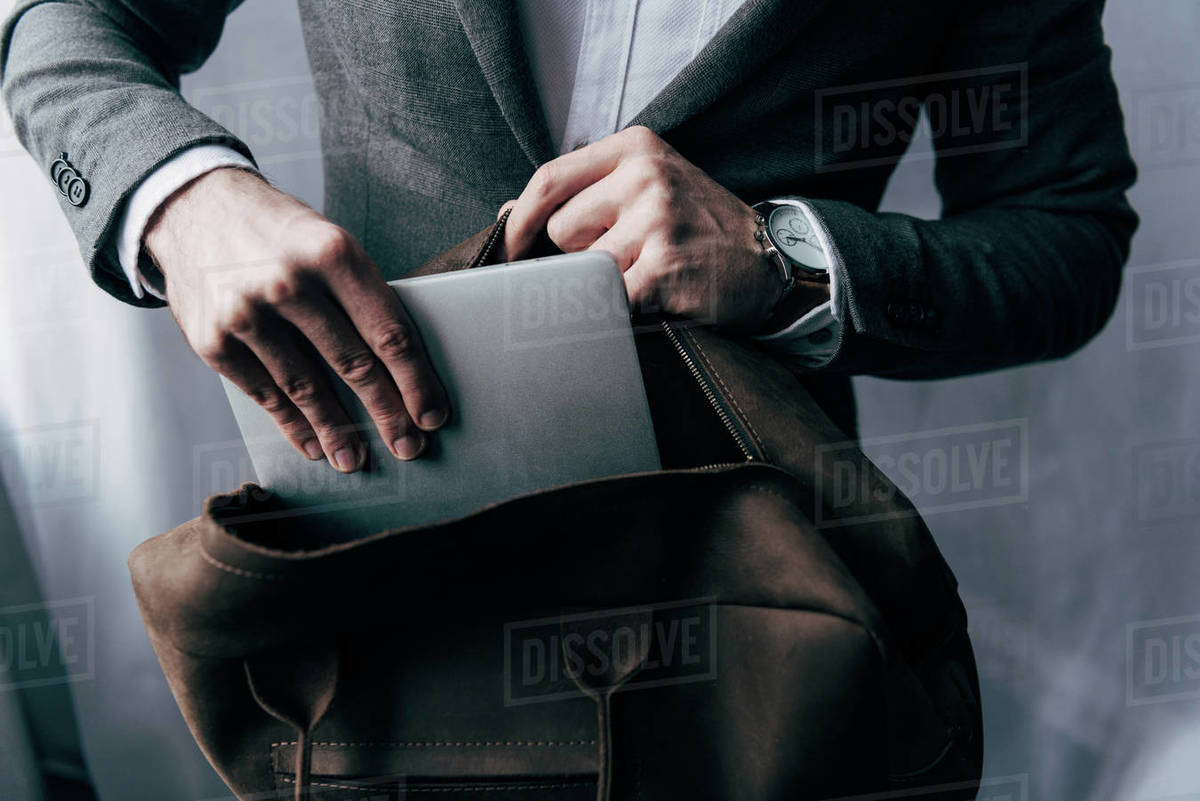 cropped image of businessman in jacket putting laptop in bag Stock