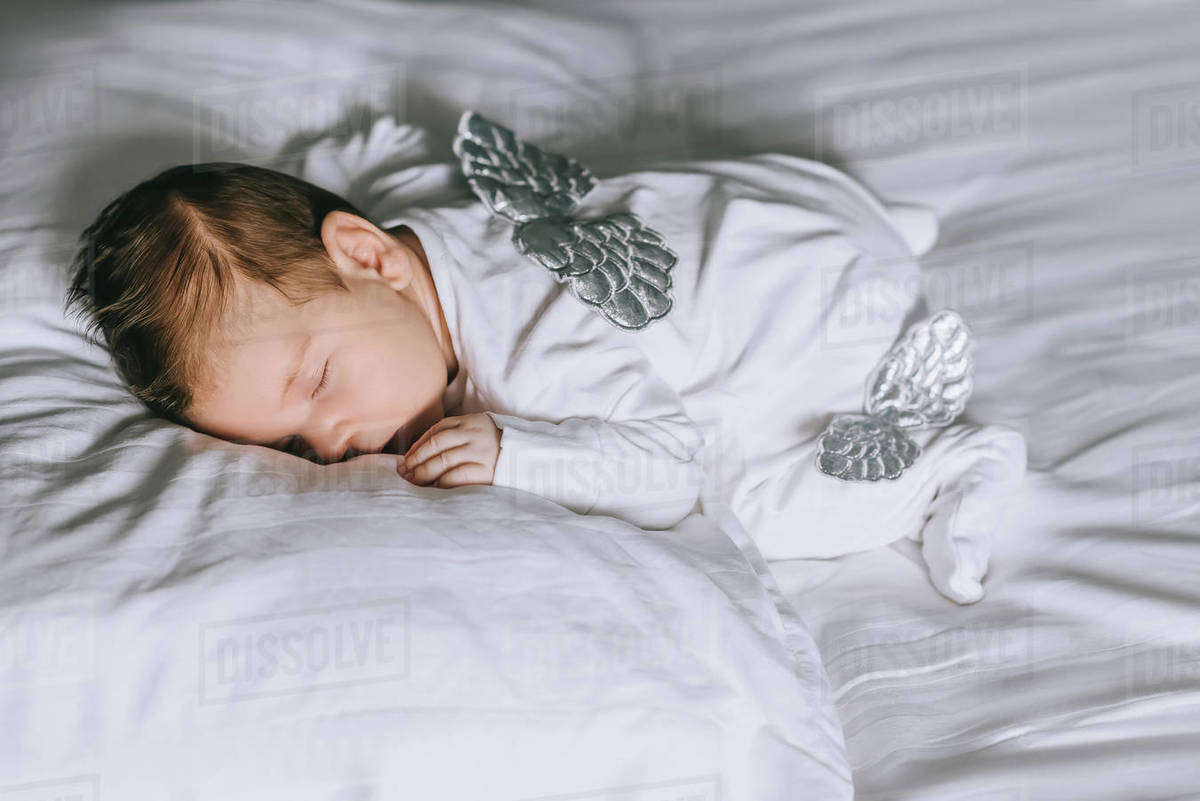 Adorable little baby boy in costume with wings sleeping in bed at home