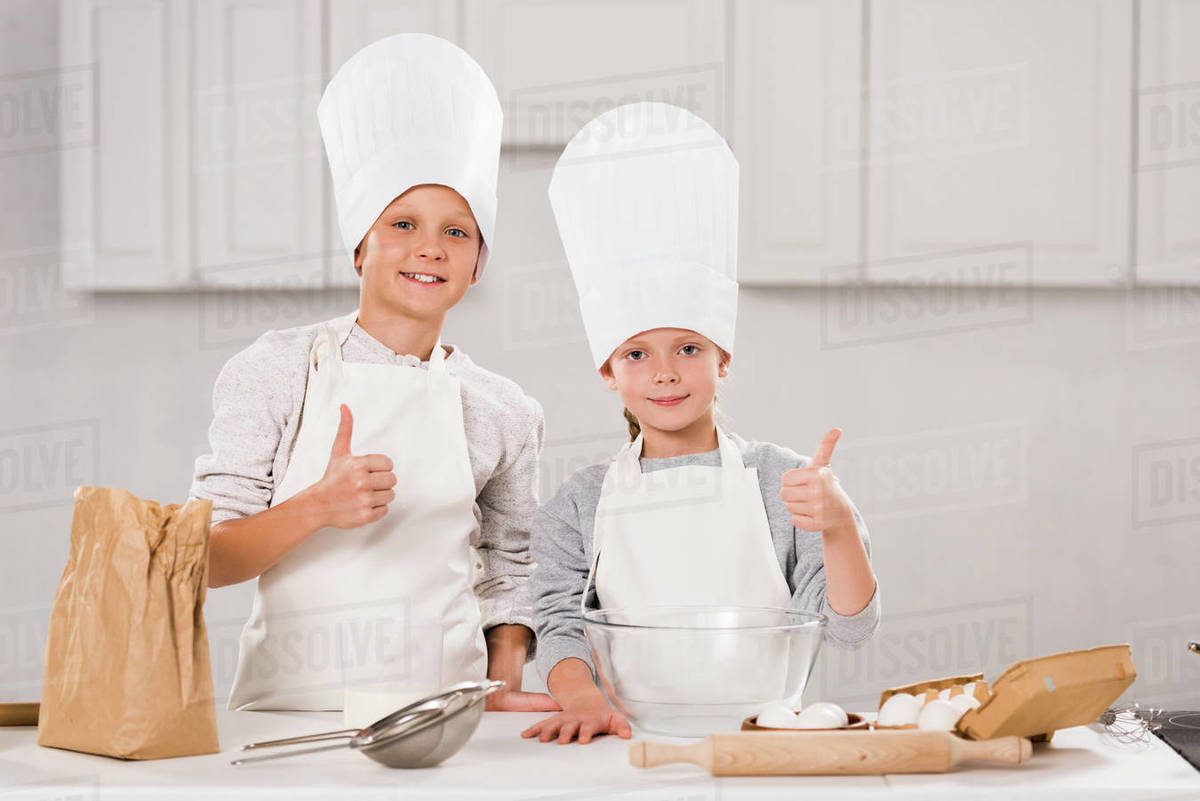 adorable brother and sister in chef hats showing thumbs up during food
