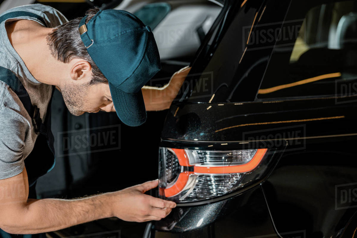 Side view of young auto mechanic checking car back headlamp at auto