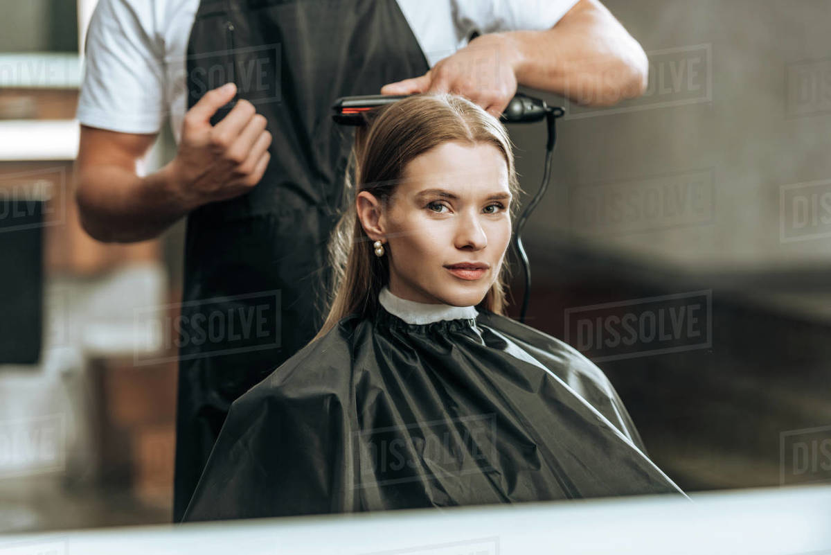 Cropped Shot Of Hairstylist Using Hair Straightener And Girl