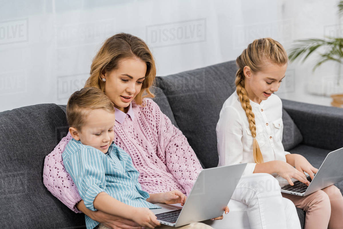 Attractive woman with children sitting on sofa and using laptops in