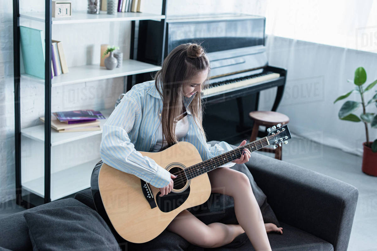 Musician sitting on sofa and playing acoustic guitar in living room