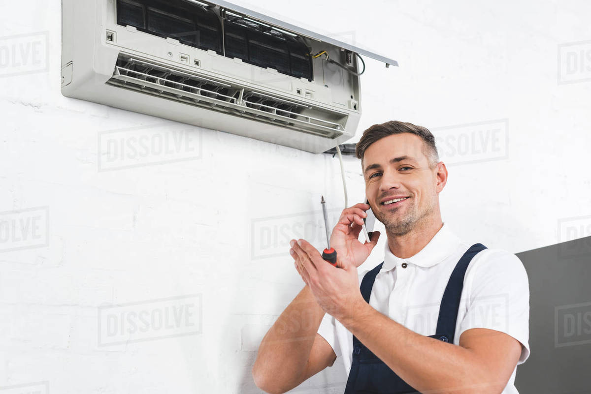 Happy man talking on smartphone while repairing air conditioner Stock