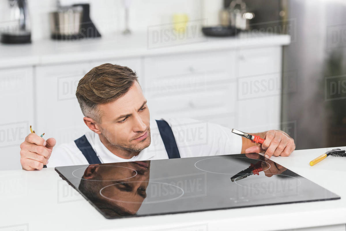 Thoughtful adult repairman repairing electric stove at kitchen Stock