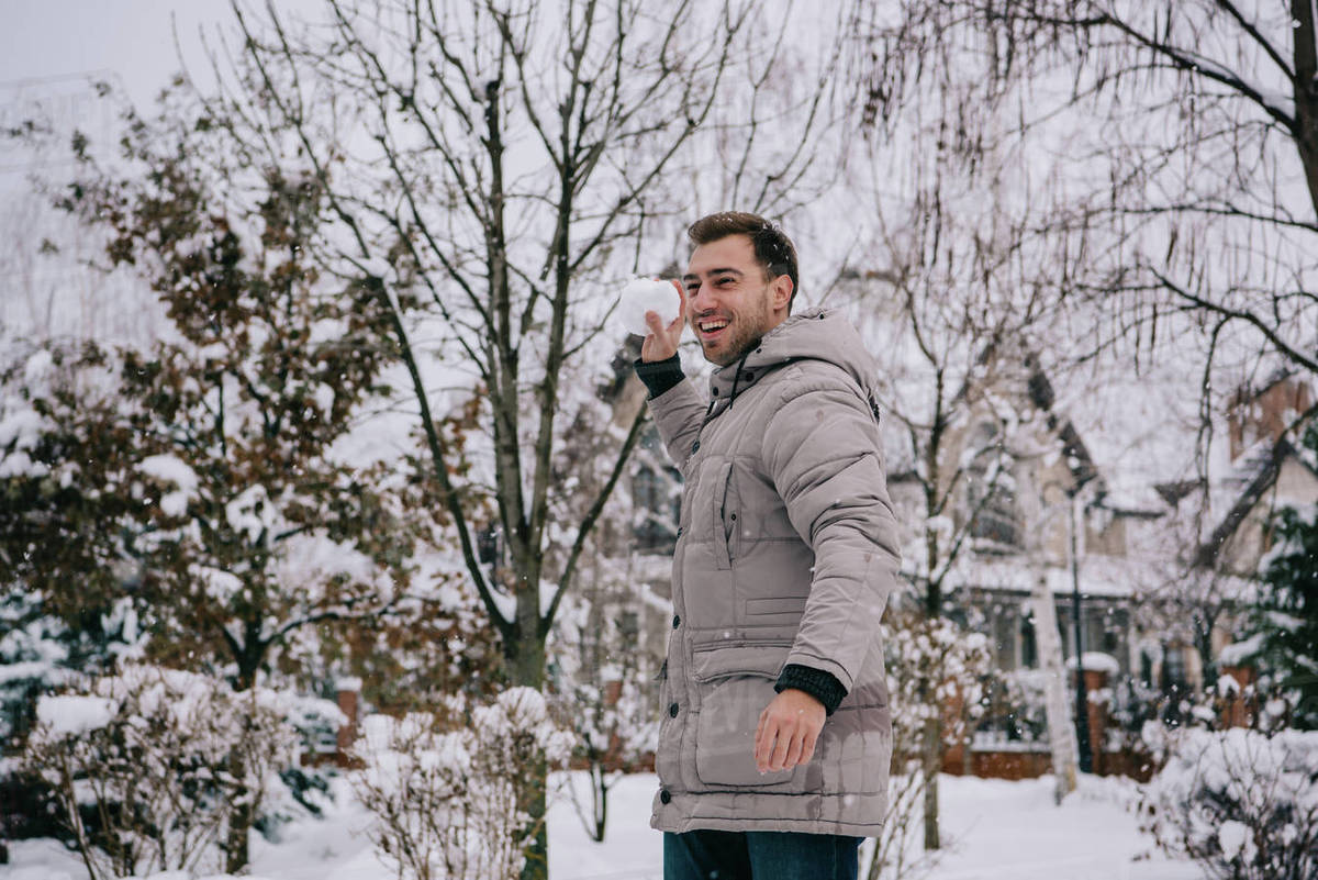 Cheerful man throwing snowball in winter Stock Photo Dissolve