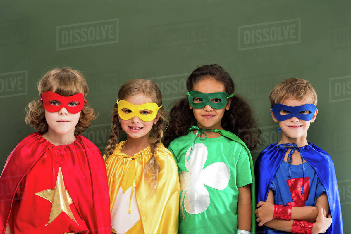 Little pupils in colorful superhero costumes, chalkboard behind Stock