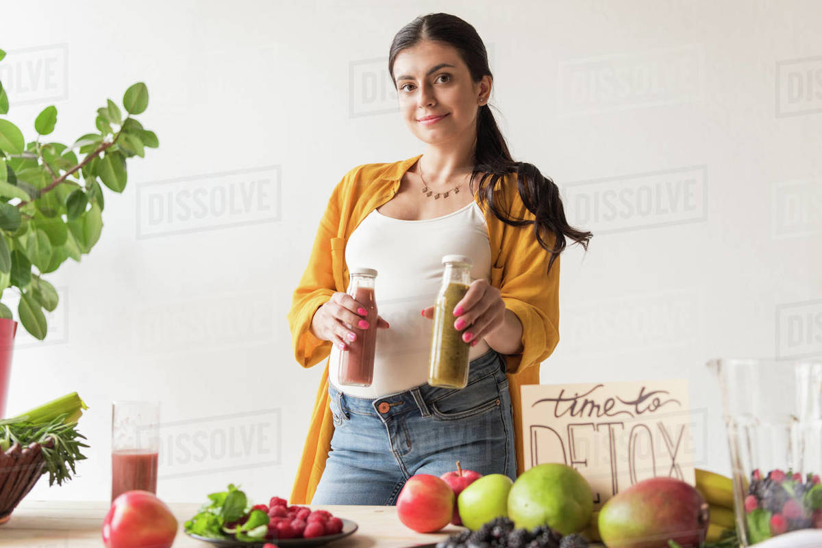 Portrait of beautiful pregnant woman with detox drinks in hands looking