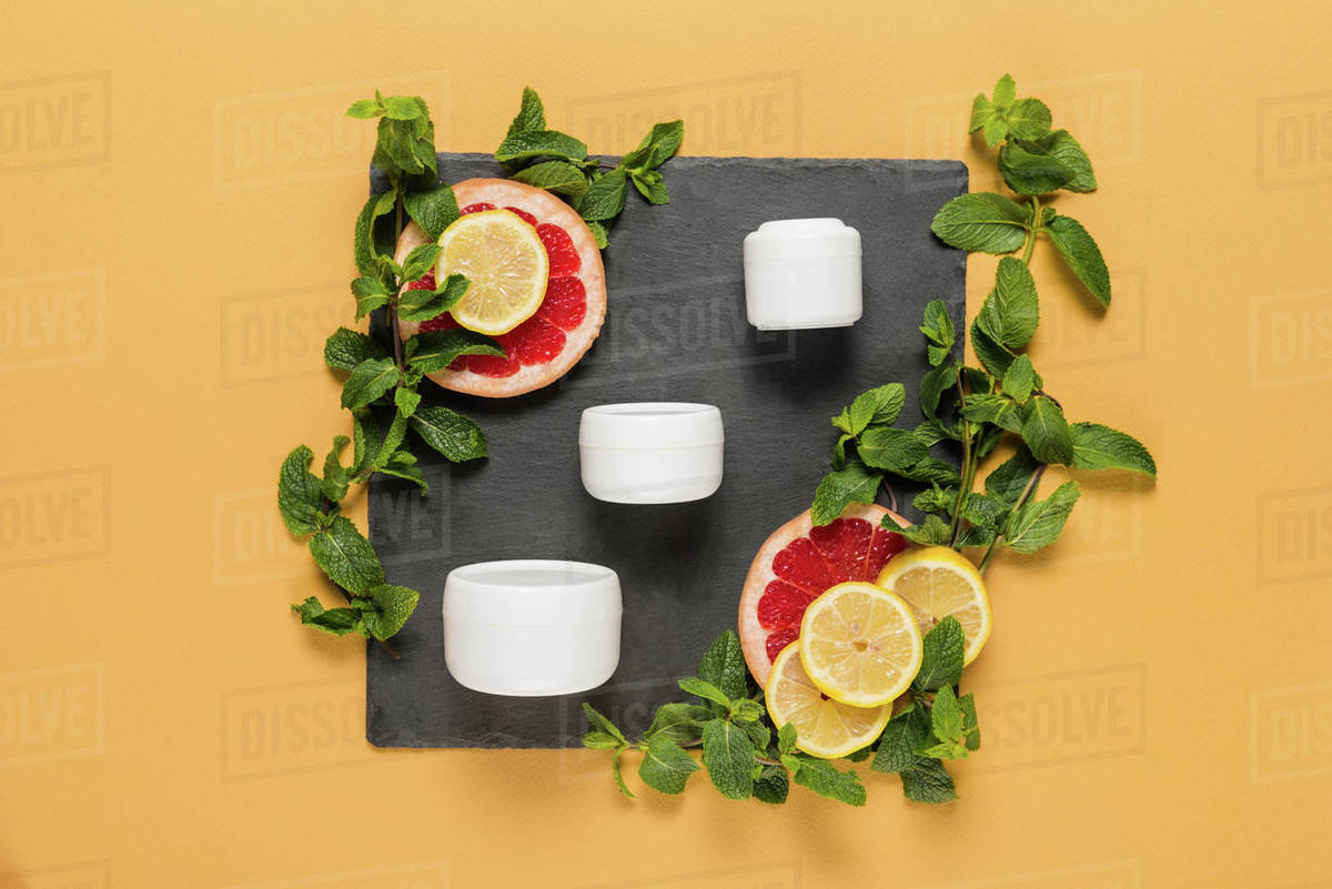 Organic citrus cream in plastic containers with mint leaves, lemon and grapefruit slices on